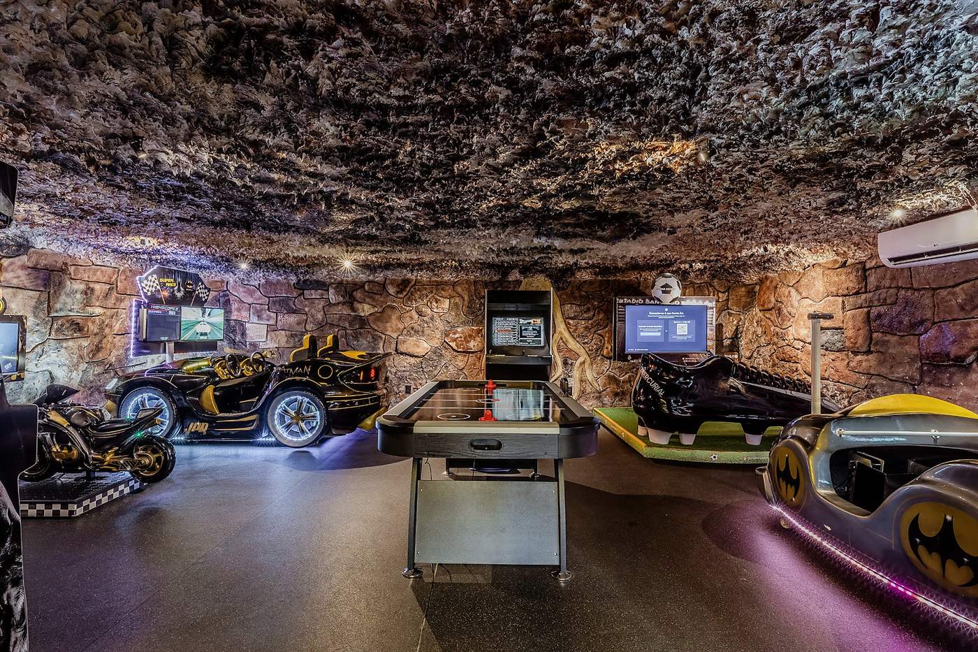 Gruta de eletrônicos da TRYBOO, com fliperamas e mesa de air hockey em uma sala de paredes de pedra